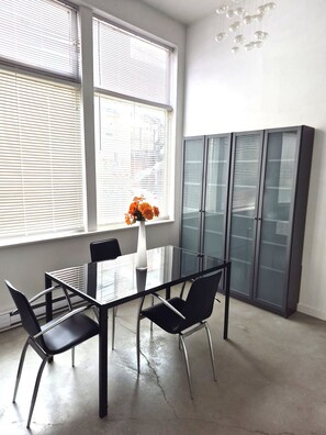 Ein moderner Konferenzraum mit Glastisch, schwarzen Stühlen, einer Vase mit orangenen Blumen und einem grauen Schrank mit Glastüren.