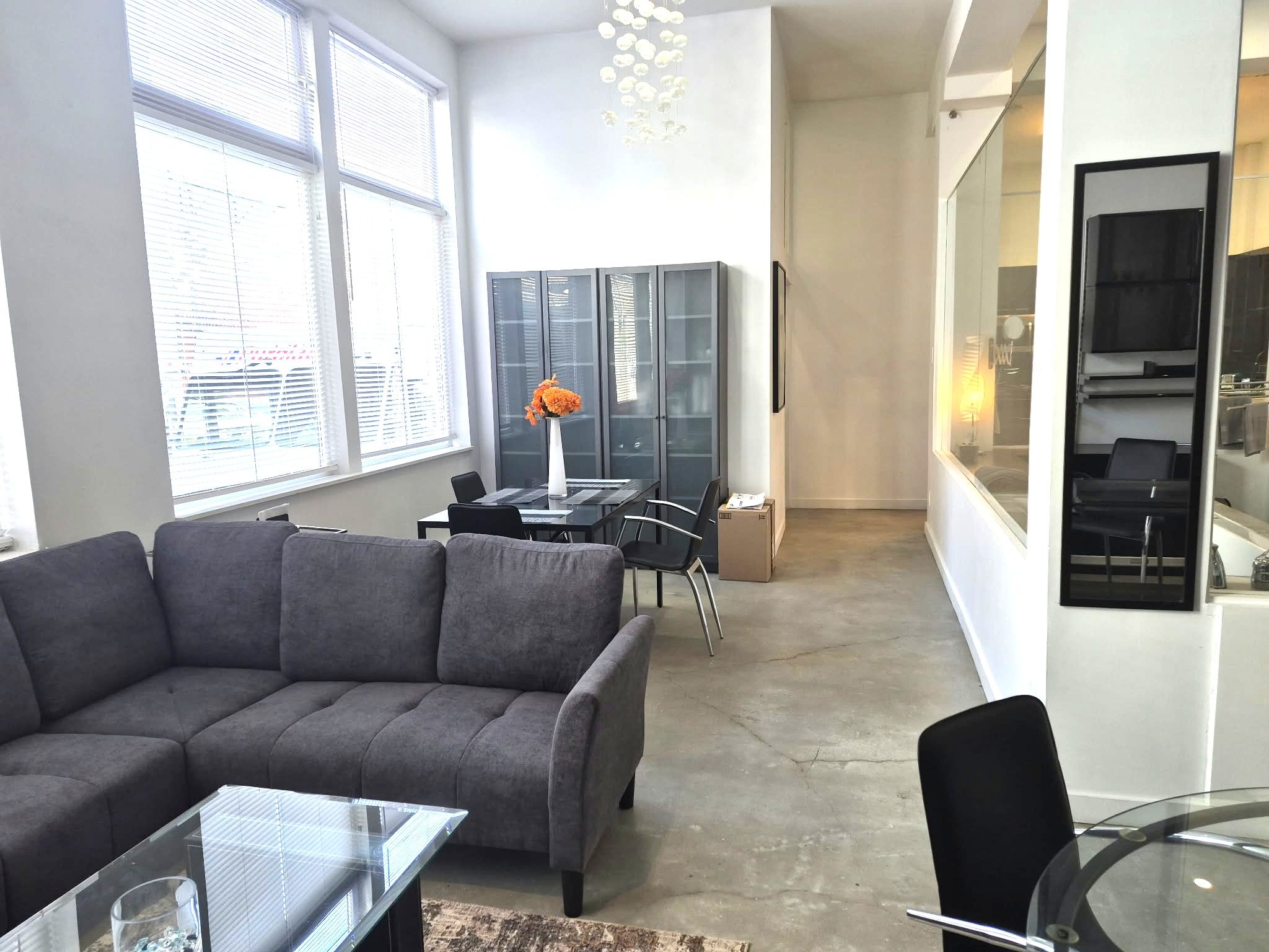 Una sala de estar moderna con un sofá gris, una mesa de centro de vidrio y un comedor con una mesa y sillas.