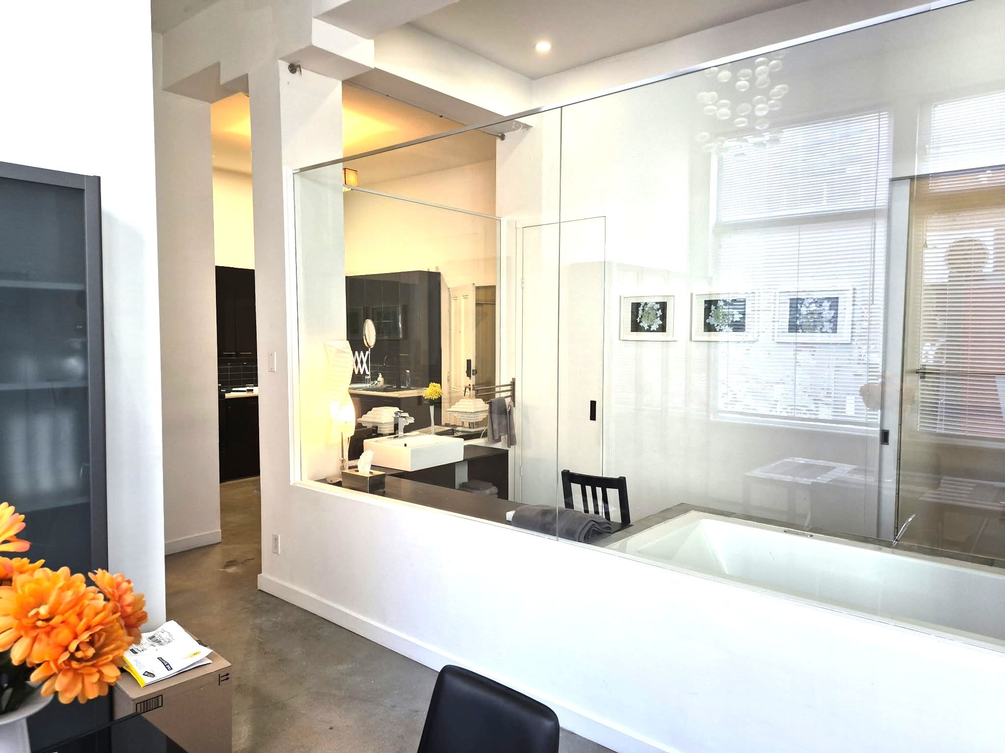 A modern bathroom with a glass partition, a sink, a mirror, and a chair.