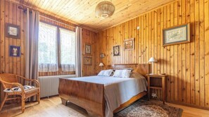 A wooden-paneled room with a bed, a chair, a nightstand, and a window with curtains. - La Pruneyre - ESPINCHAL (ESPINCHAL)