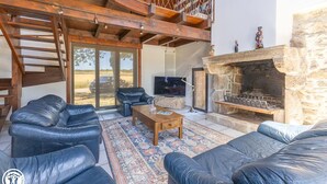 Ein modernes Wohnzimmer mit Ledersofas, einem Holztisch, einem Kamin aus Naturstein und einem Fernseher.