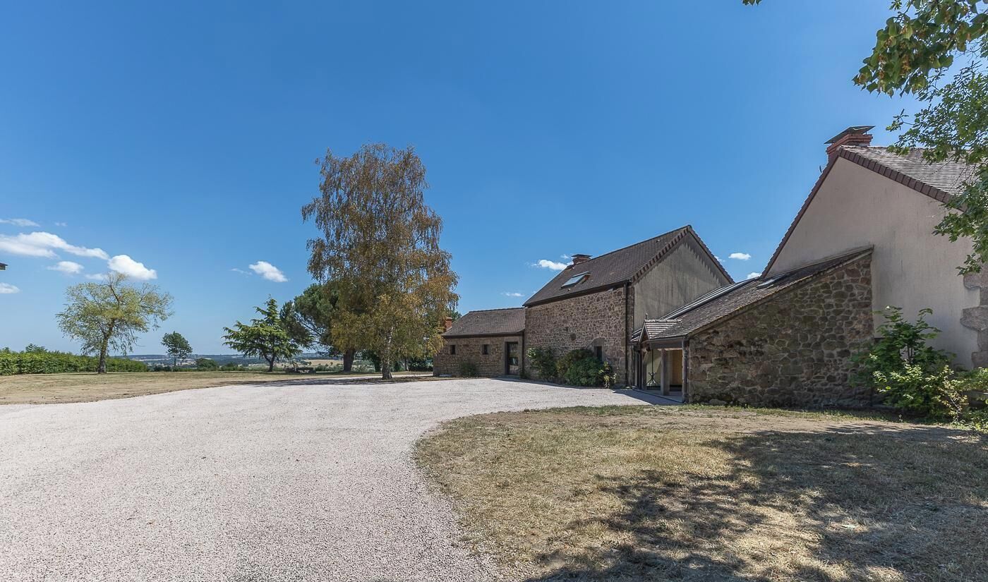 A stone building with a gravel driveway and a large tree in front.