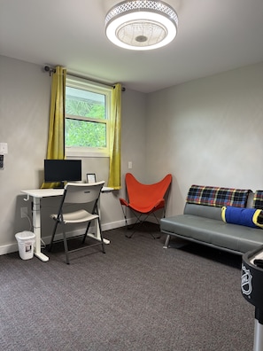Una habitación con escritorio, silla y sofá con manta.