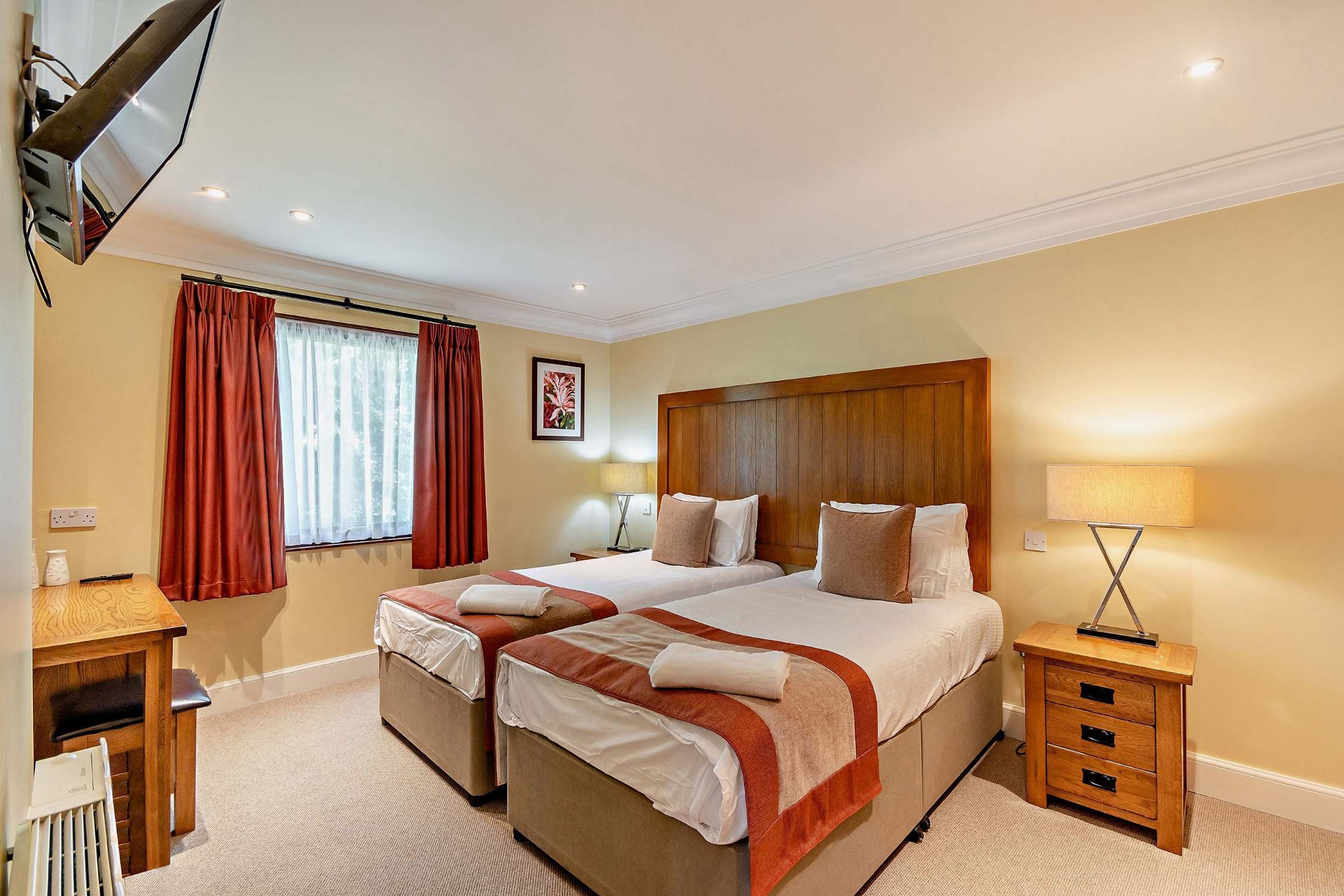 A hotel room with two beds, a desk, a chair, a lamp, and a window with curtains.