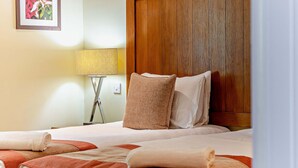 Een hotelkamer met een houten hoofdeinde, een bed met twee kussens, een bedlampje en een ingelijste foto aan de muur.