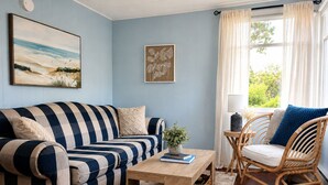 Ein Wohnzimmer mit einem gestreiften Sofa, einem Holztisch, einem Korbstuhl und einem Fenster mit Vorhängen.