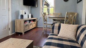 Ein Wohnzimmer mit Fernseher, Holzmöbeln, einem Esstisch mit Stühlen und einem Fenster mit Aussicht.
