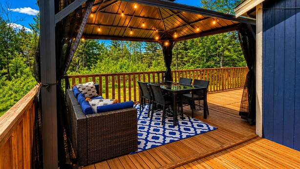 Eine überdachte Terrasse im Freien mit Tisch, Stühlen, einer Couch und einem gemusterten Teppich.