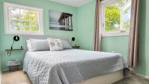 Ein Schlafzimmer mit einem Bett, zwei Nachttischen, einer Wandleuchte, einem Bild und einem Fenster mit Vorhängen.