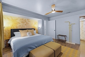Ein Schlafzimmer mit einem Bett, einer Bank, einem Deckenventilator und einer Wand mit tropischem Wandpapier.