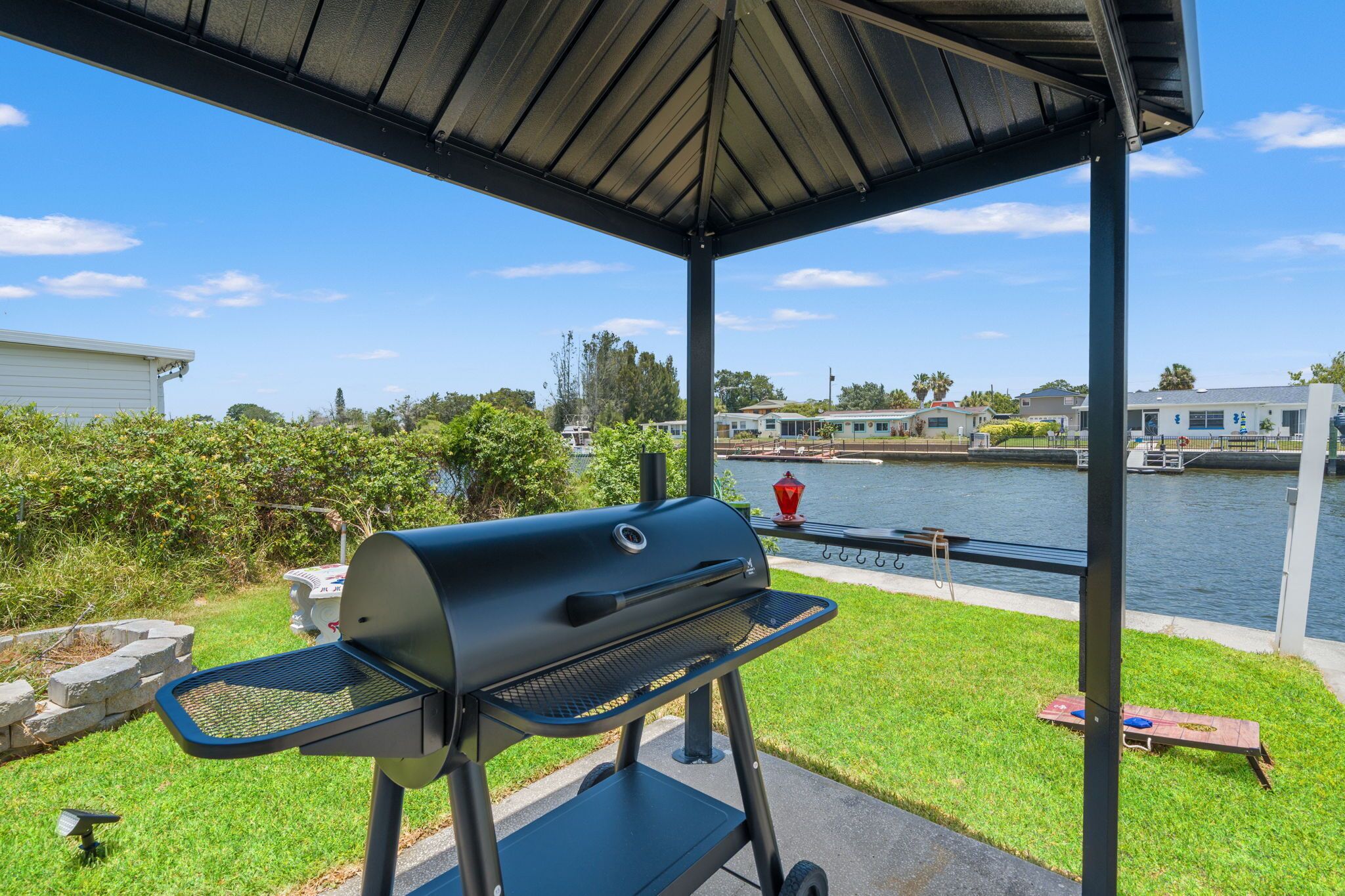 Een overdekt grillgedeelte met uitzicht op een gracht en huizen op de achtergrond.