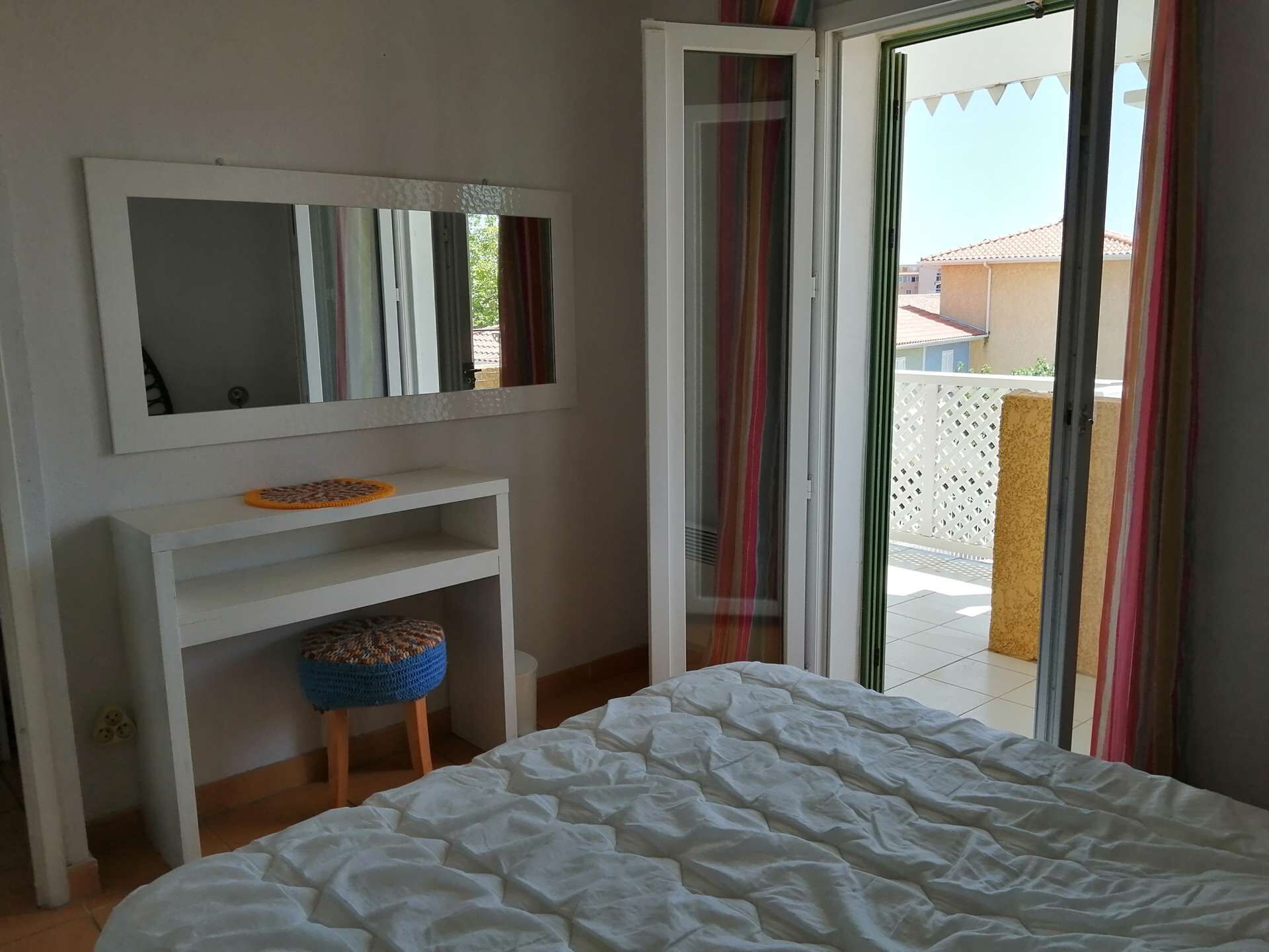 Een slaapkamer met een bed, een spiegel, een klein krukje en een schuifdeur die uitkomt op een buitenruimte.