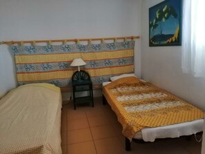 Ein Zimmer mit zwei Betten, einem Sessel, einer Lampe und einem Bild an der Wand.