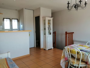 Ein Zimmer mit Fliesenboden, einem weißen Schrank mit Glastüren, einem hölzernen Stuhl, einem Tisch mit bunten Tischdecken und einer Kristallleuchtre.