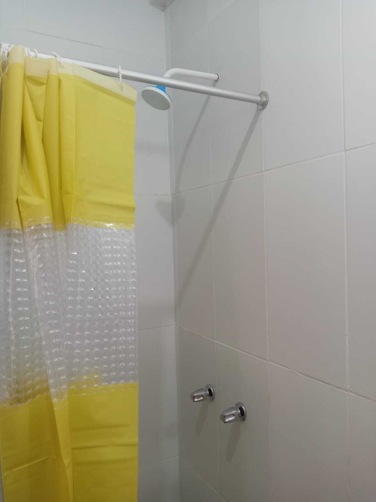 Área de duche com cortina amarela, chuveiro manual e parede revestida a azulejos.