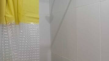 Área de duche com cortina amarela, chuveiro manual e parede revestida a azulejos.