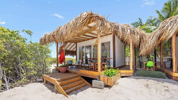 A beachside bungalow with a thatched roof, a wooden deck, and a small outdoor seating area. - Hideaway Aruba: Private Villa with Jacuzzi (Savaneta)