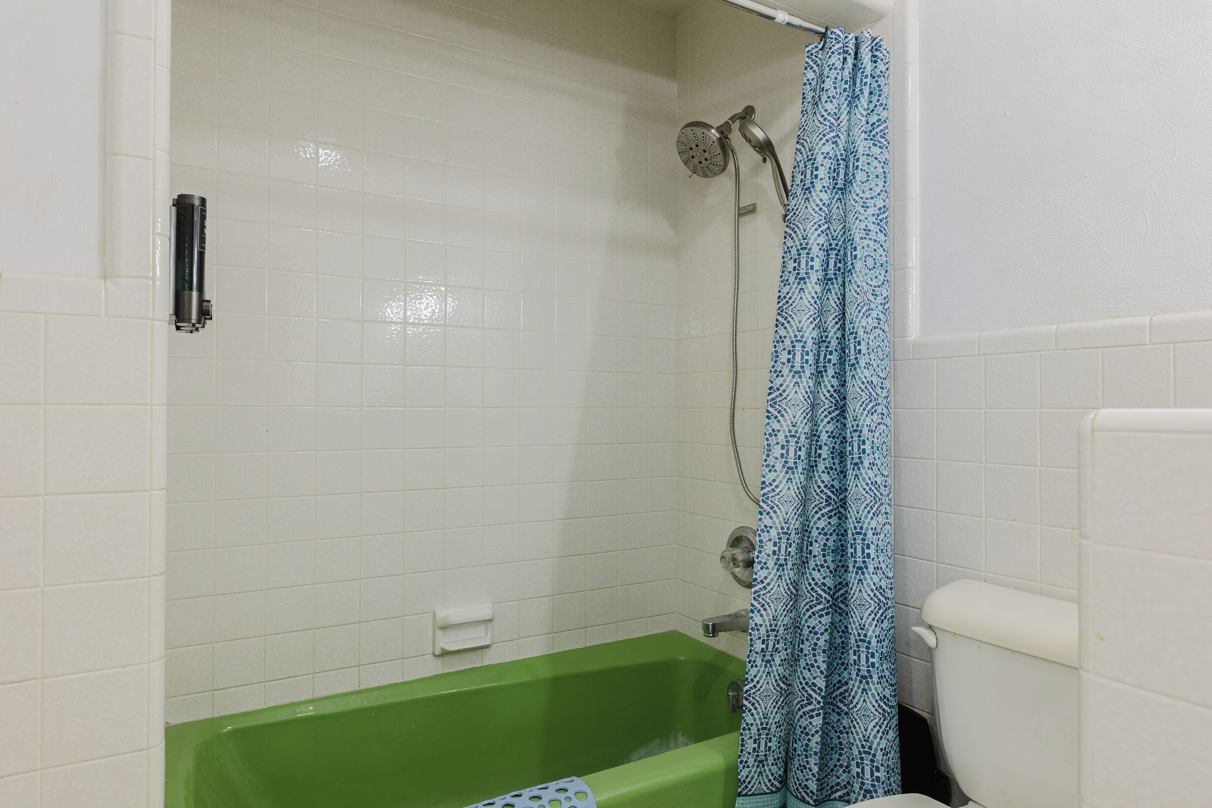 Een badkamer met een groen bad, een douche met een blauw patroon gordijn en een wit toilet.