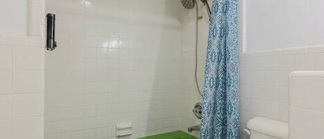 Een badkamer met een groen bad, een douche met een blauw patroon gordijn en een wit toilet.