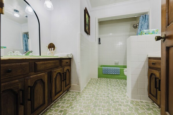 Une salle de bain avec un meuble-lavabo en bois, une baignoire verte et une zone de douche carrelée de blanc.