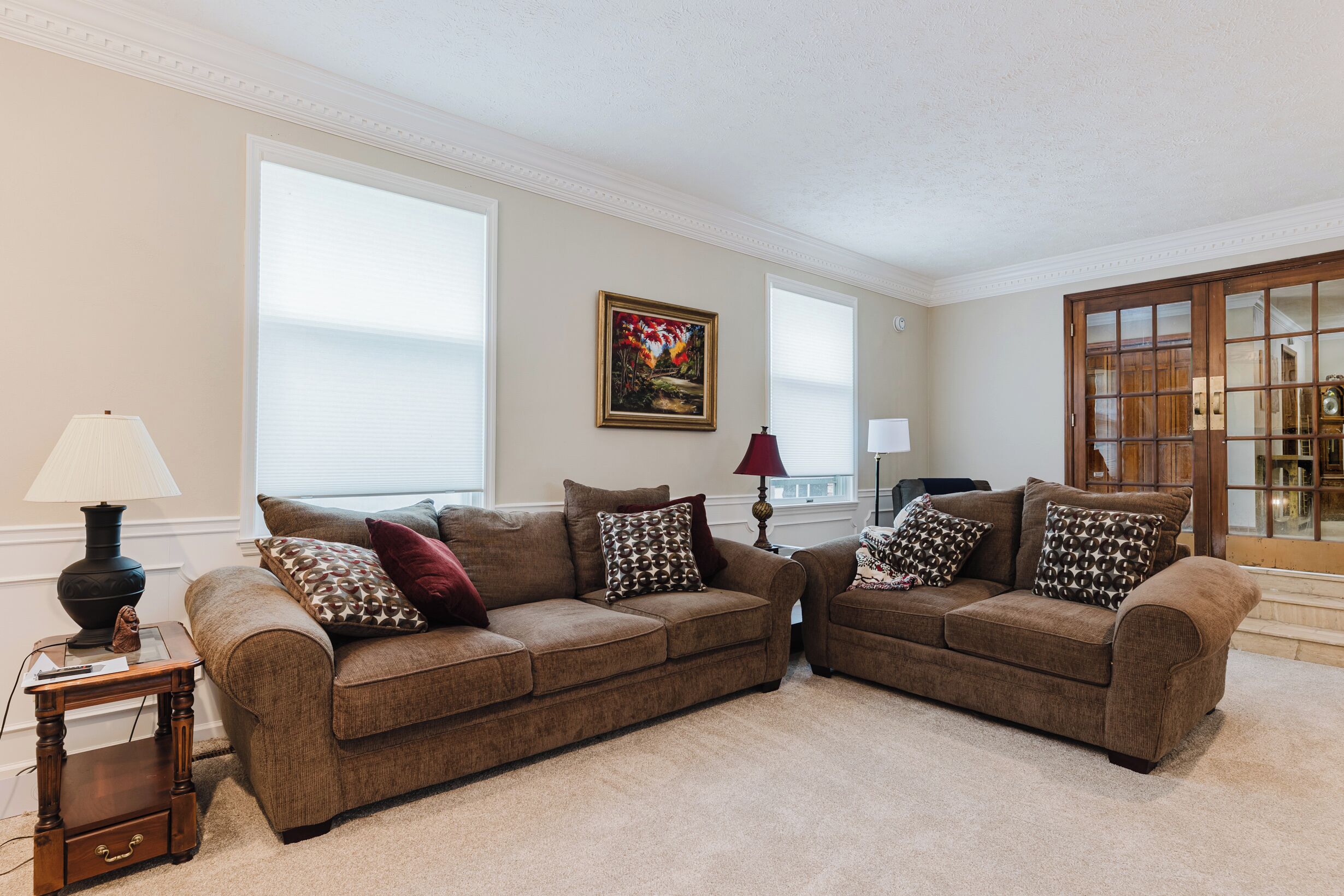 A living room with two brown sofas, a small wooden side table, a lamp, and a painting on the wall.