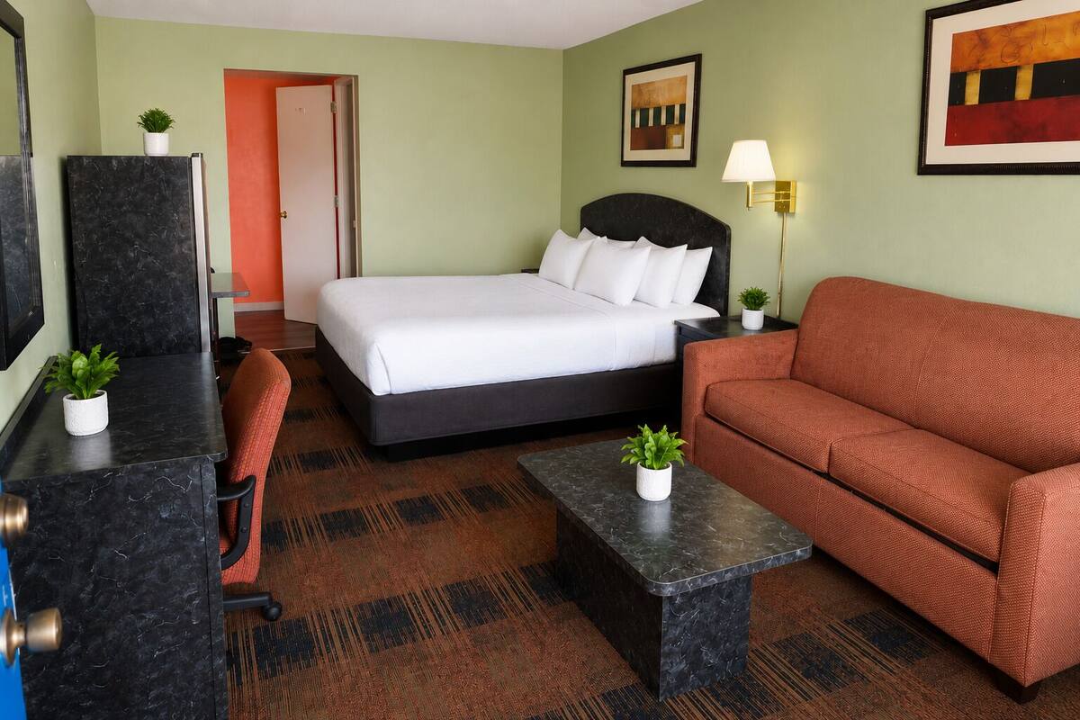 Una habitación de hotel con cama, sofá, escritorio, silla y lámpara.