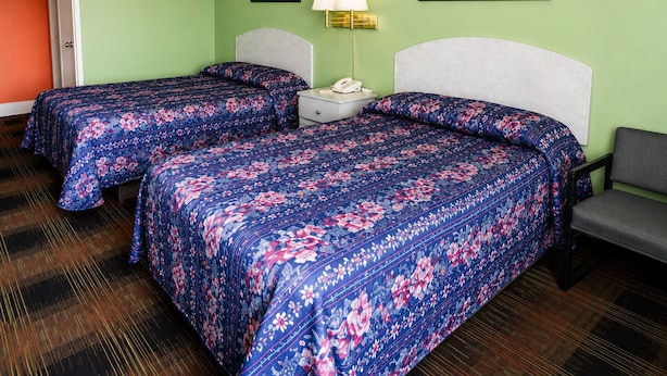 Quarto de hotel com duas camas, uma mesinha de cabeceira com abajur e um quadro na parede.