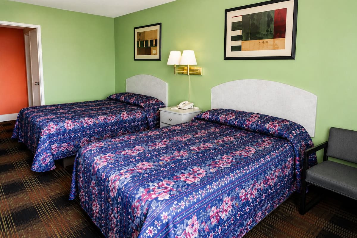 Habitación de hotel con dos camas, una mesita de noche con lámpara y un cuadro enmarcado en la pared.
