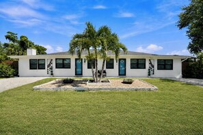 A single-story house with a well-maintained lawn, a small garden with palm trees, and a clear blue sky. - Nokomis Sunset Retreat w/Patio 8 mins to  Beach (Nokomis)