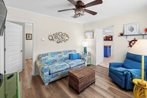 A living room with a blue sofa, a wicker ottoman, a ceiling fan, and a wall-mounted clock. - Nokomis Sunset Retreat w/Patio 8 mins to  Beach (Nokomis)