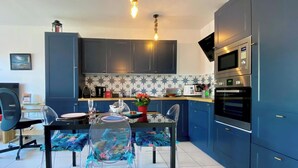 Uma cozinha moderna com armários escuros, uma sala de jantar com mesa de vidro e uma televisão na sala de estar.
