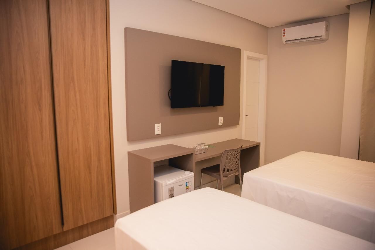 Una habitación de hotel con cama, escritorio, silla, televisor y armario.