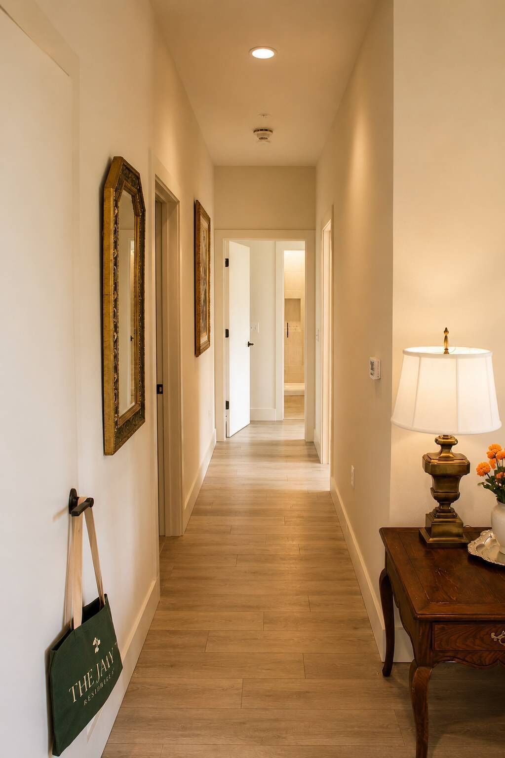 A hallway with wooden flooring, a lamp, and a framed mirror on the wall.
