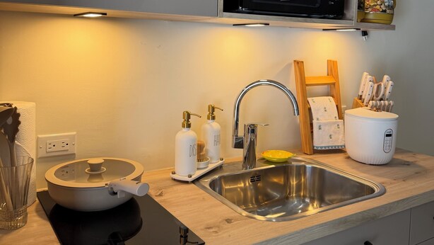 A modern kitchen with a built-in microwave, a sink, and a wooden shelf above. - Boutique Studio | King Bed & Pool | Unit 1 | Aluna (Savaneta)