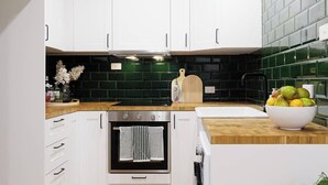 Uma cozinha moderna com armários brancos, painel de azulejos pretos, bancada de madeira e pia branca.
