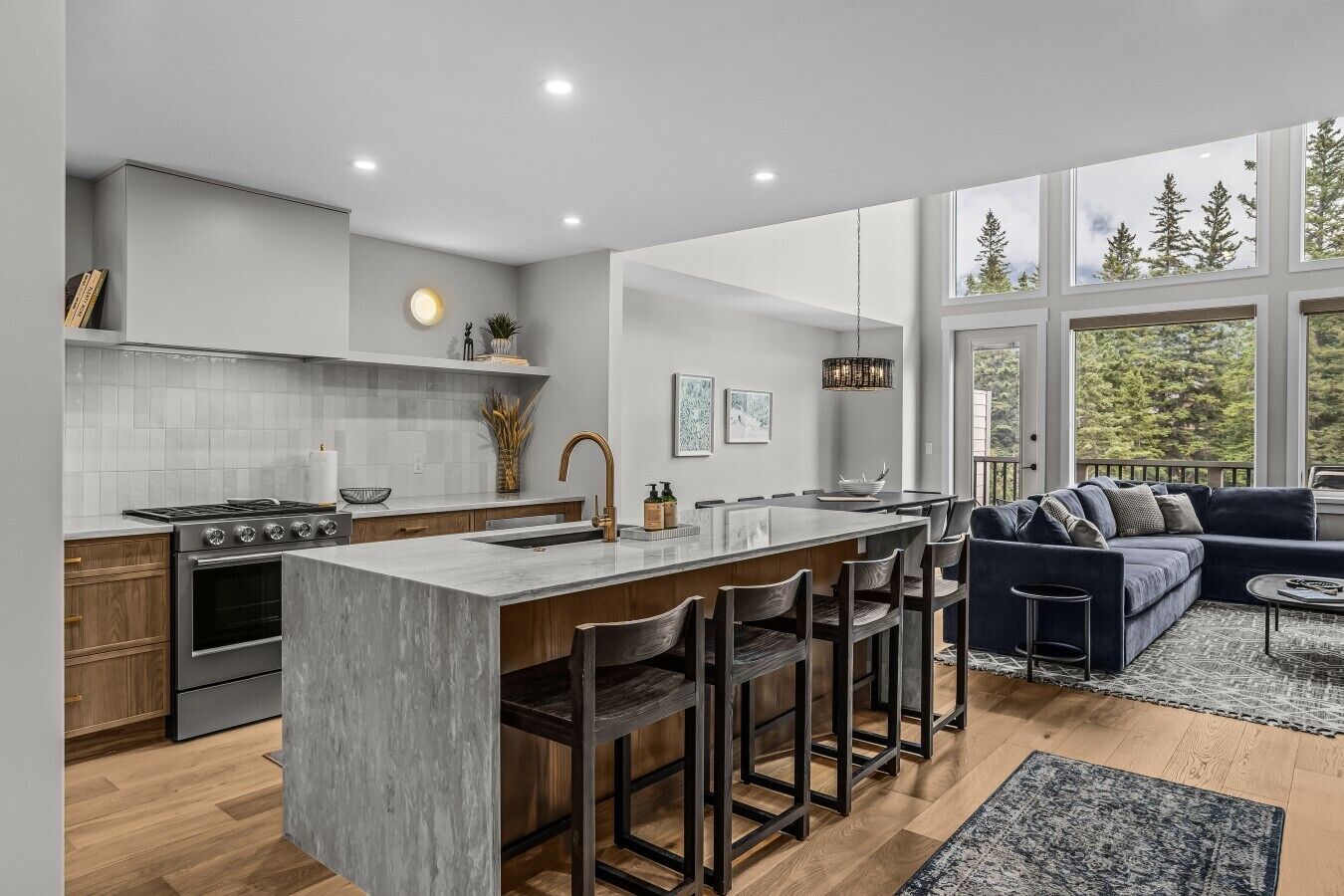 A modern kitchen with a large island, wooden cabinets, and a dining area with a dark blue sofa.