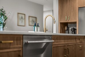A kitchen with a stainless steel dishwasher, wooden cabinets, a gold faucet, and two framed pictures on the wall.