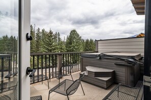 A balcony with a hot tub, outdoor seating, and a view of trees.