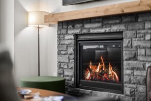 A fireplace with a stone facade and a visible fire, a green ottoman, and a floor lamp. - Walk to Town | Luxury Home with Private Hot Tub (Canmore)