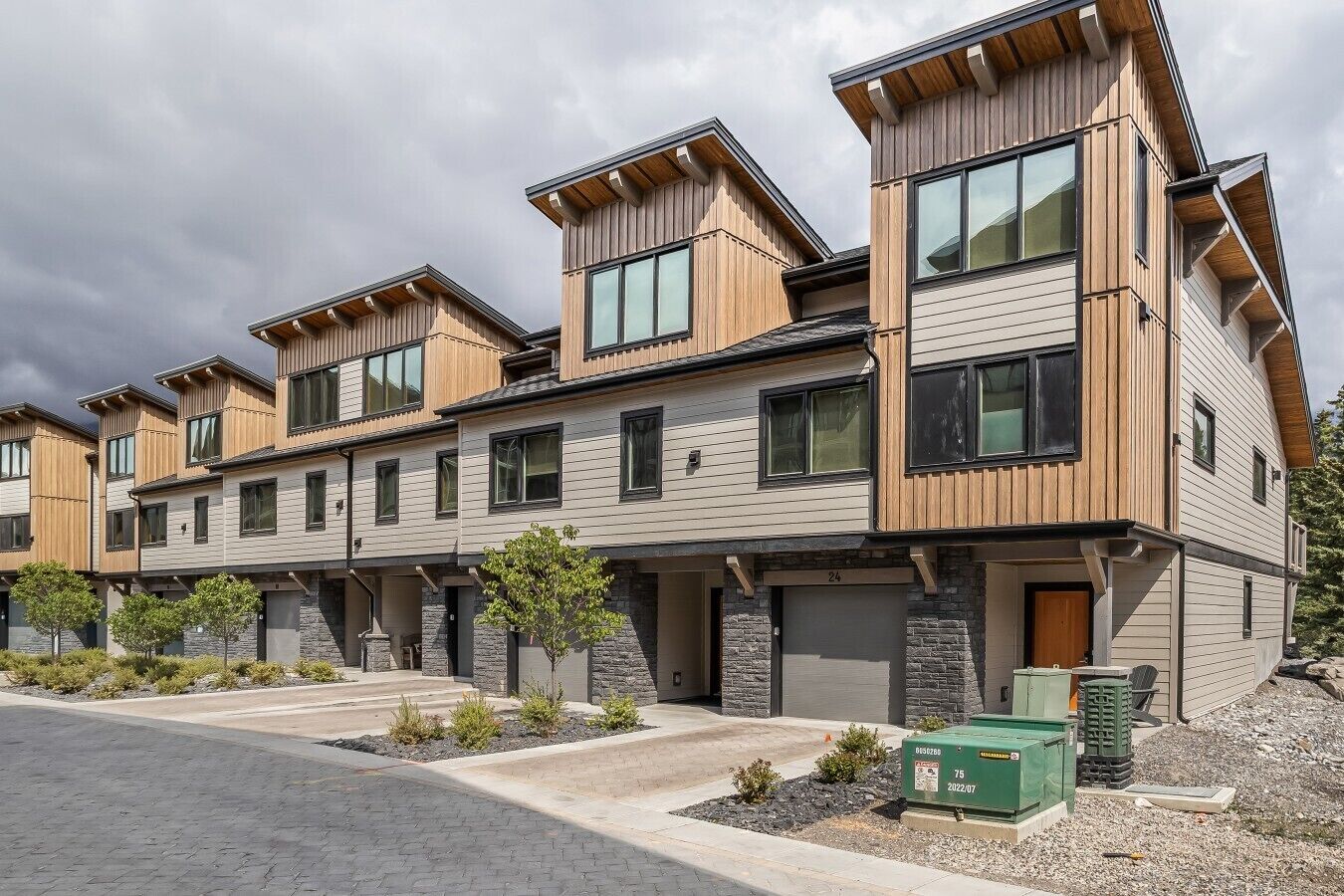 A modern multi-story residential building with a mix of wood and stone exterior, numbered 24, featuring a front entry with a door and windows.