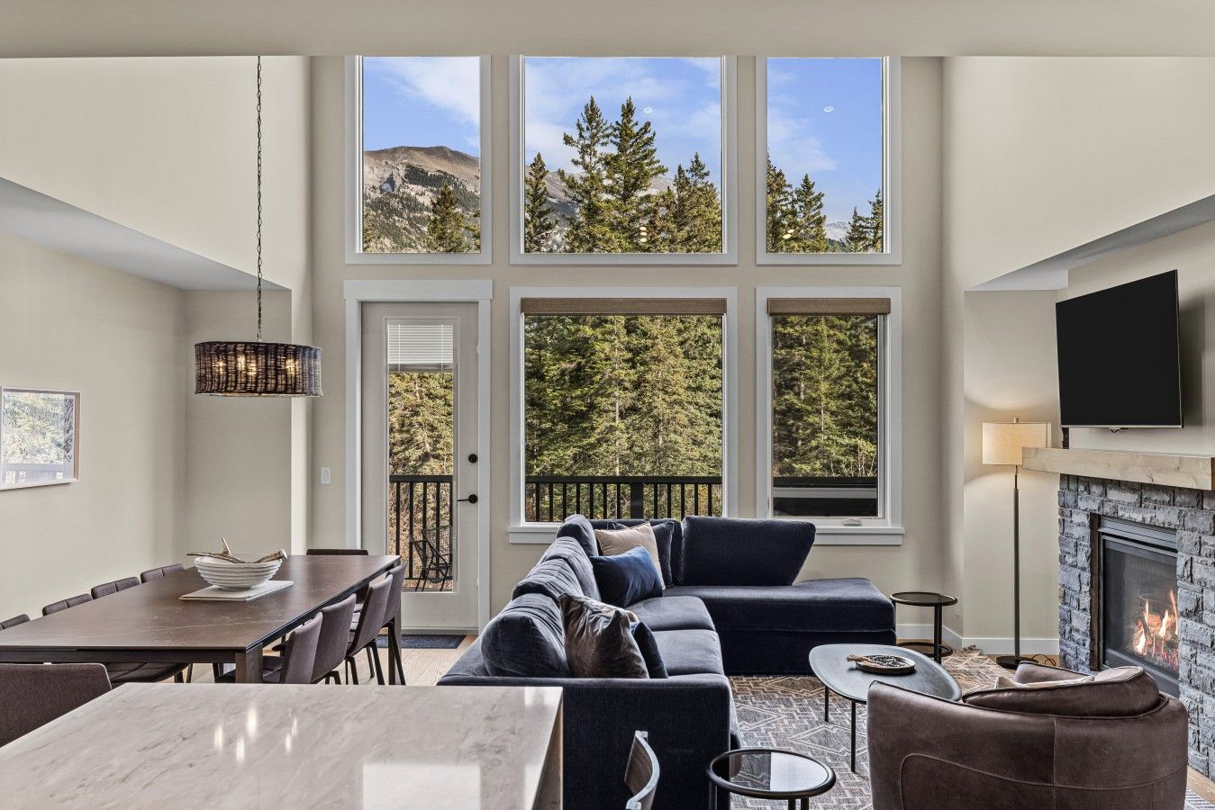 A modern living room with a fireplace, large windows, and a dining area.
