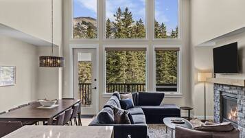 A modern living room with a fireplace, large windows, and a dining area.