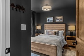 A bedroom with a wooden bed, two bedside lamps, a ceiling light, and two framed pictures on the wall.