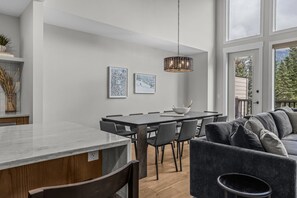 A modern dining area with a large table, chairs, and a hanging light fixture. - Walk to Town | Luxury Home with Private Hot Tub (Canmore)