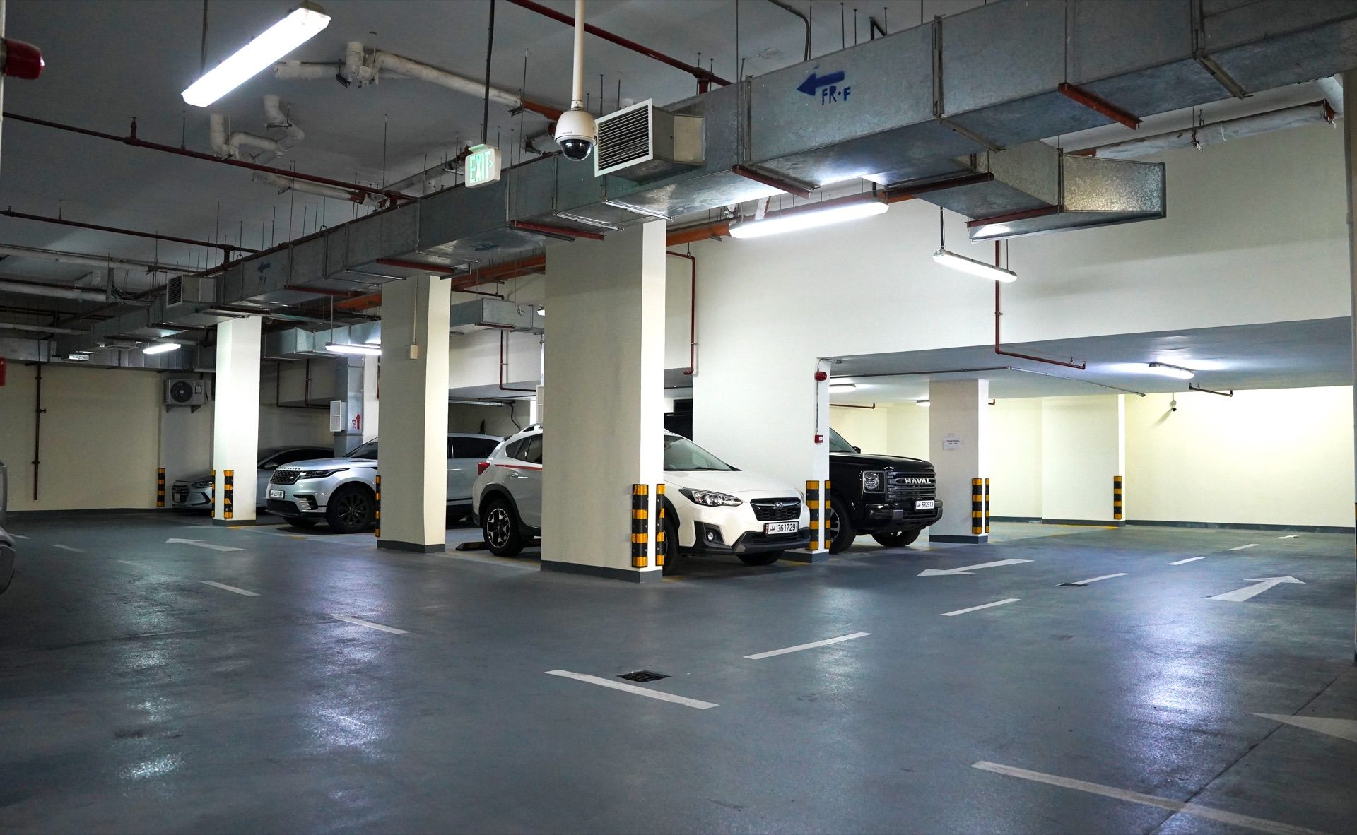 Un estacionamiento con varios niveles y varios autos estacionados, con señales de salida visibles y columnas estructurales.
