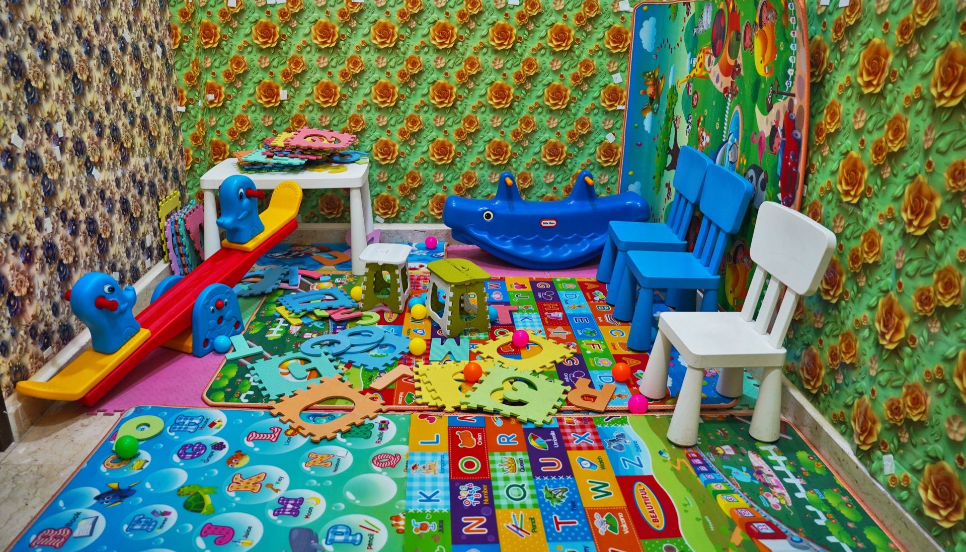 Una sala de juegos con un tapete de alfabeto colorido, un tobogán y varios juguetes.
