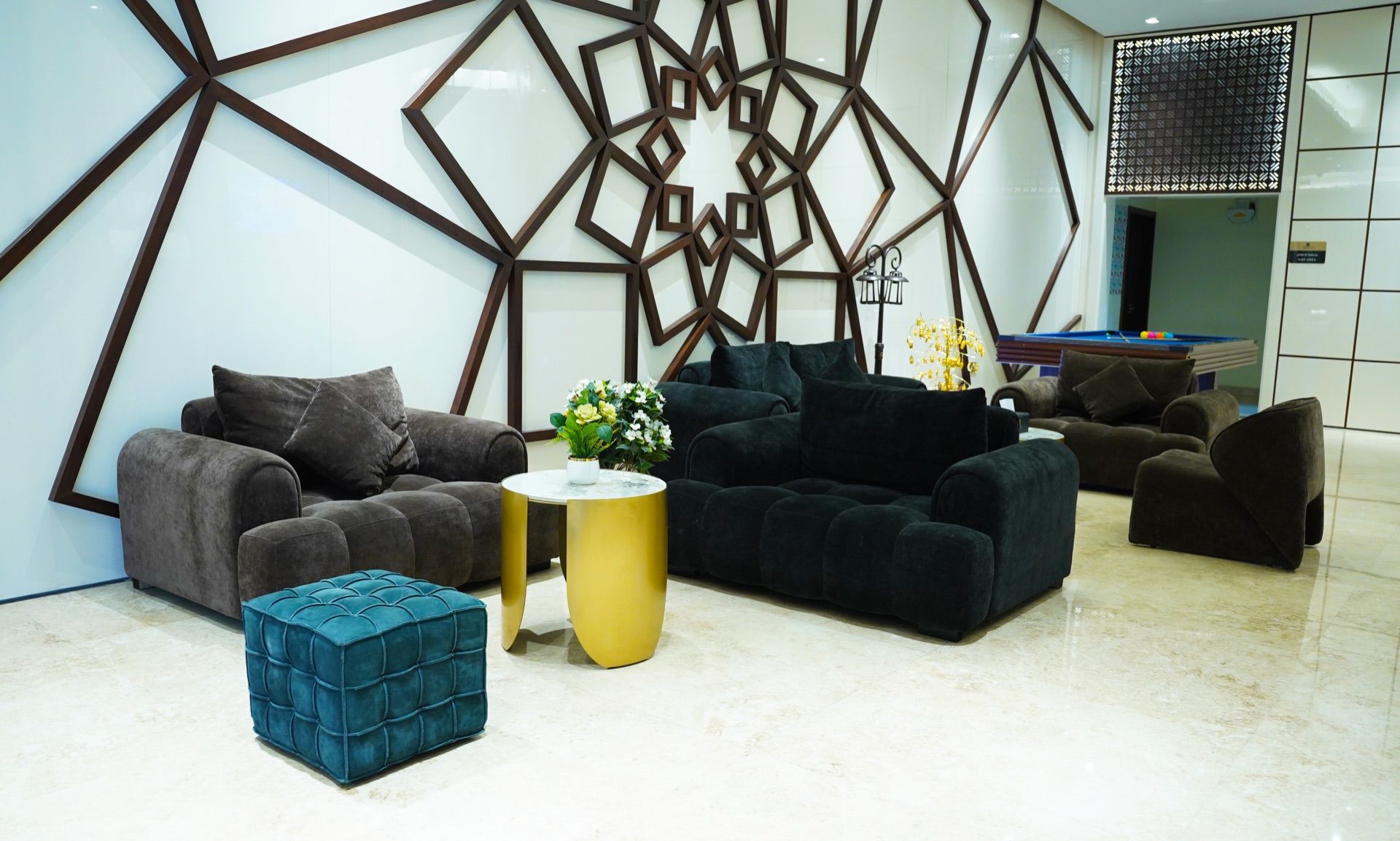 A modern living room with dark sofas, a teal ottoman, and a gold side table.