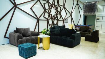 A modern living room with dark sofas, a teal ottoman, and a gold side table.