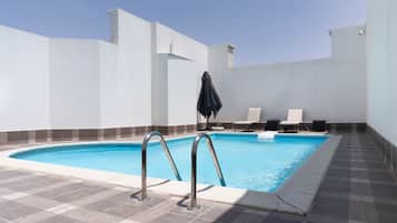 Ein Swimmingpool mit gefliestem Deck, zwei Liegestühlen und einem schwarzen Sonnenschirm.