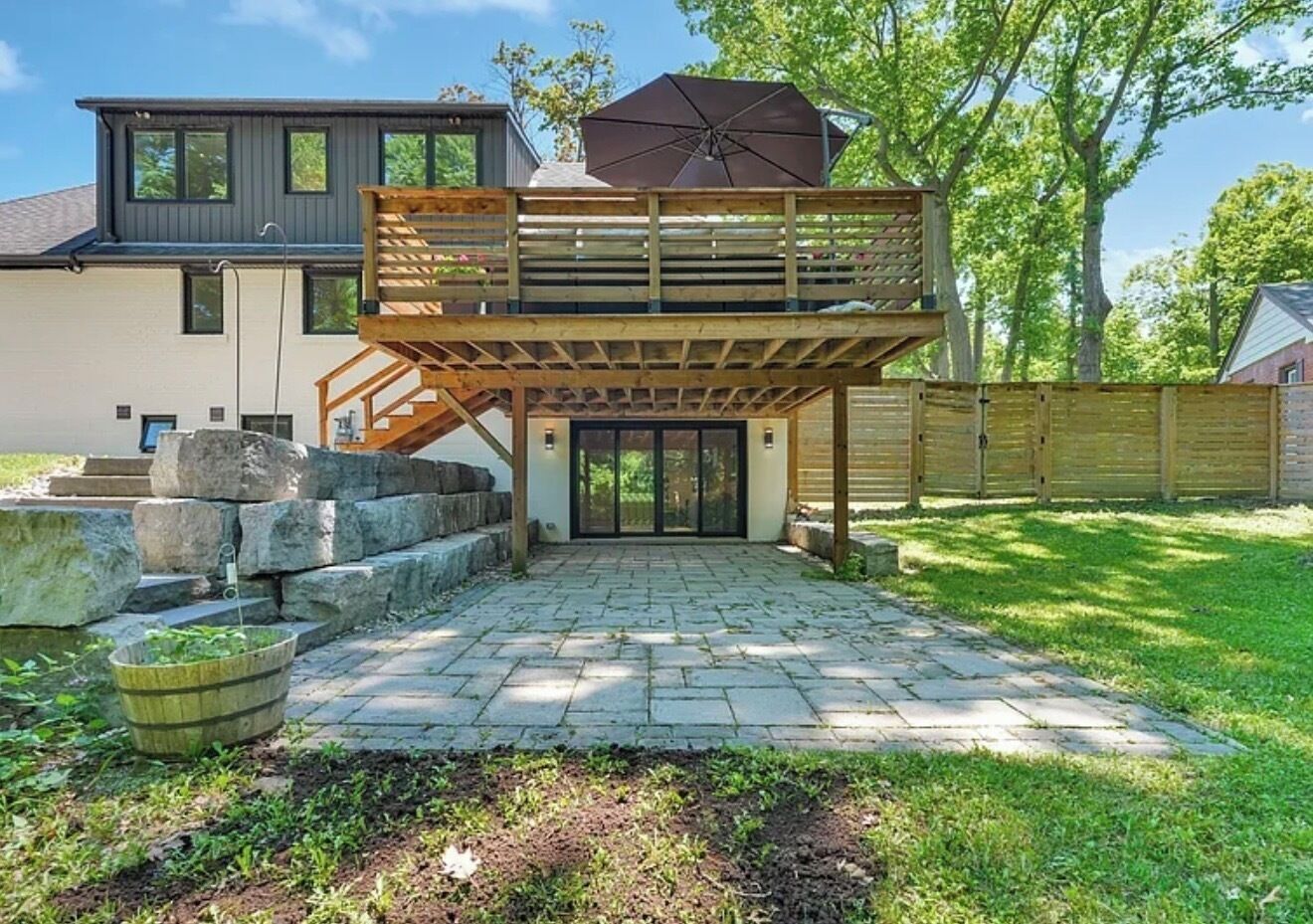 Una casa moderna con terraza de madera, una escalera que conduce a un segundo piso y un patio de piedra.